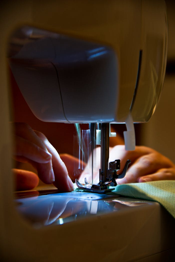 Detailed view of hands operating a sewing machine with precision lighting.