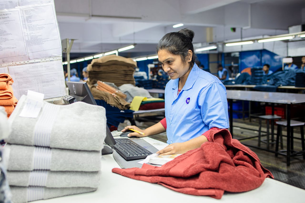 Female factory worker inspecting textiles for quality control in a busy production facility.